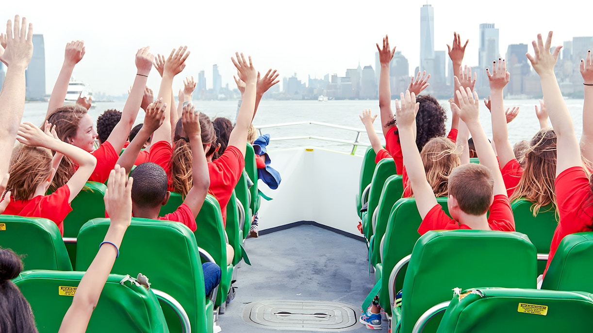 Guests raising hands on NYC speedboat ride with city skyline in view.