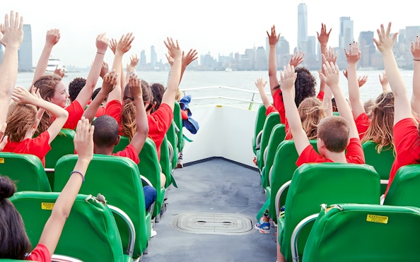 Guests raising hands on NYC speedboat ride with city skyline in view.