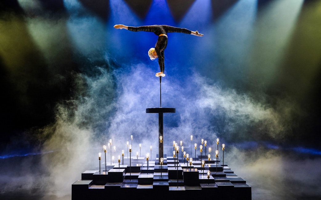 Performer balancing on one hand at Friedrichstadt Palast stage with lights and smoke effects.