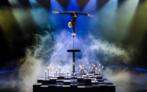 Performer balancing on one hand at Friedrichstadt Palast stage with lights and smoke effects.