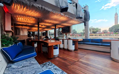 Luxurious seating area on a Nile Dahabiya dinner cruise with river view and Cairo Tower in the background.