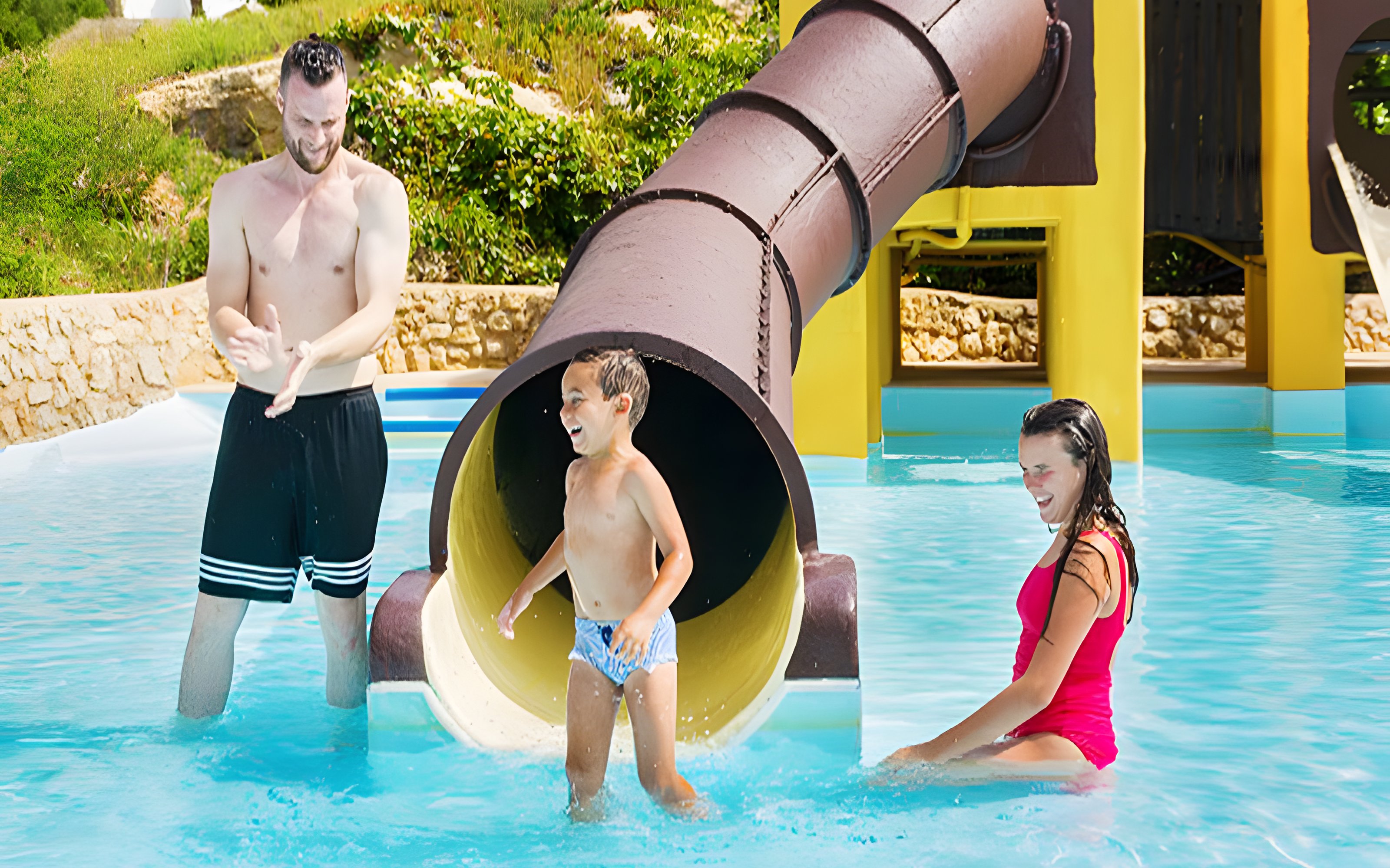 Child exiting Polynesia slide at Aquopolis Cullera water park, splashing into pool.