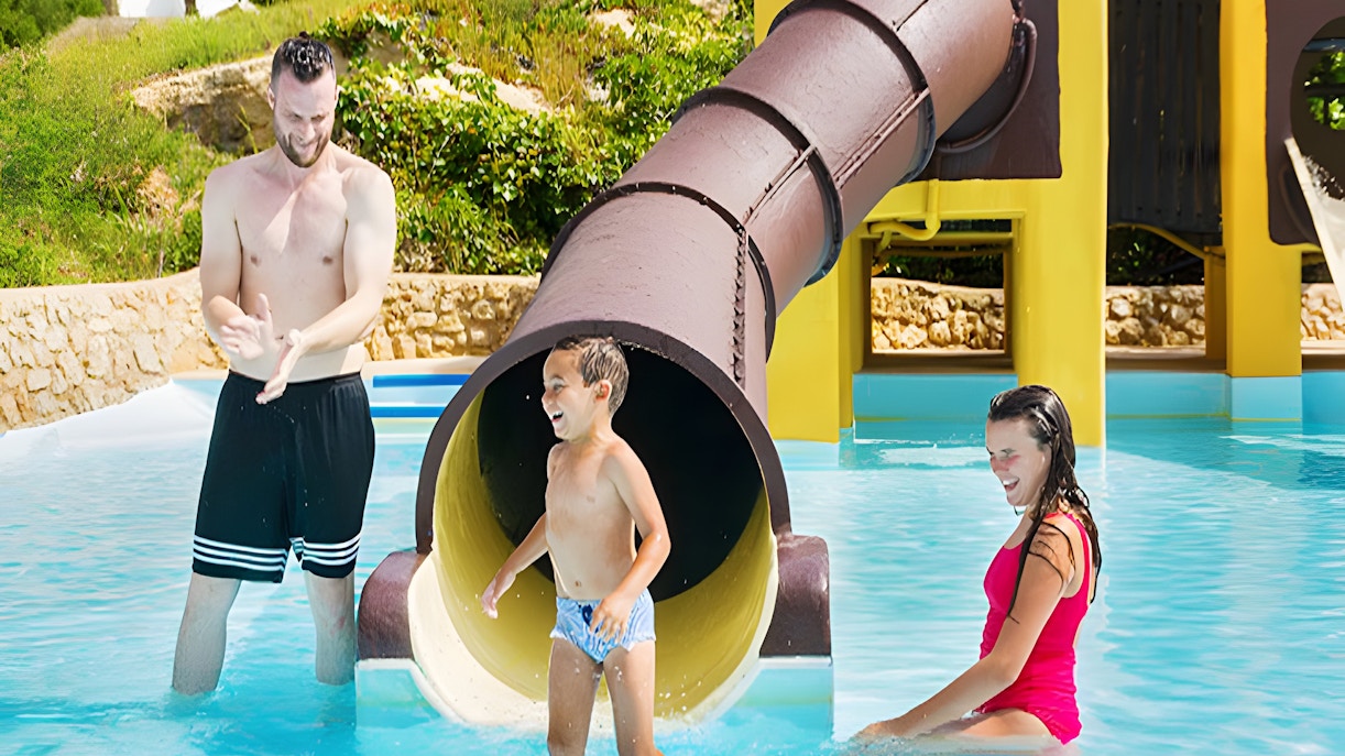 Child exiting Polynesia slide at Aquopolis Cullera water park, splashing into pool.
