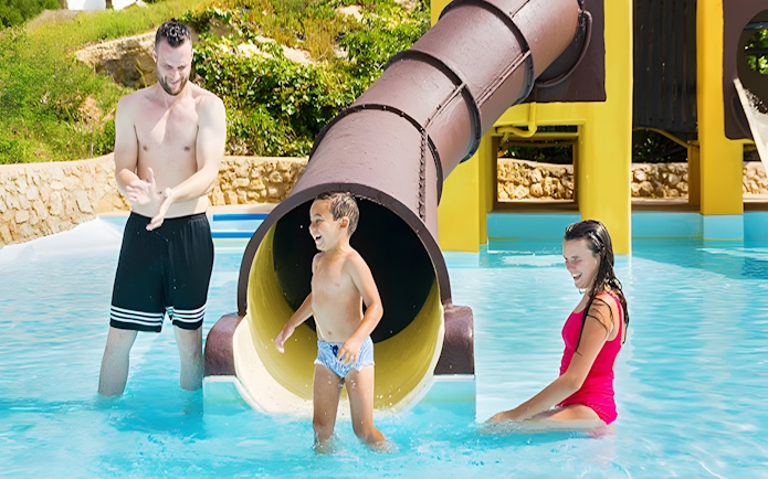 Child exiting Polynesia slide at Aquopolis Cullera water park, splashing into pool.