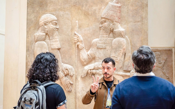 Guide explaining Assyrian relief to tourists at Louvre Museum, France.