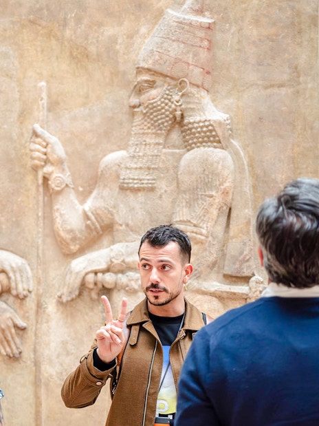Guide explaining Assyrian relief to tourists at Louvre Museum, France.