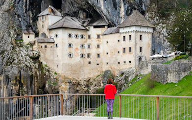 Predjama Castle built into a cliff with a visitor on the viewing platform.