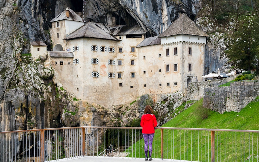 Predjama Castle built into a cliff with a visitor on the viewing platform.