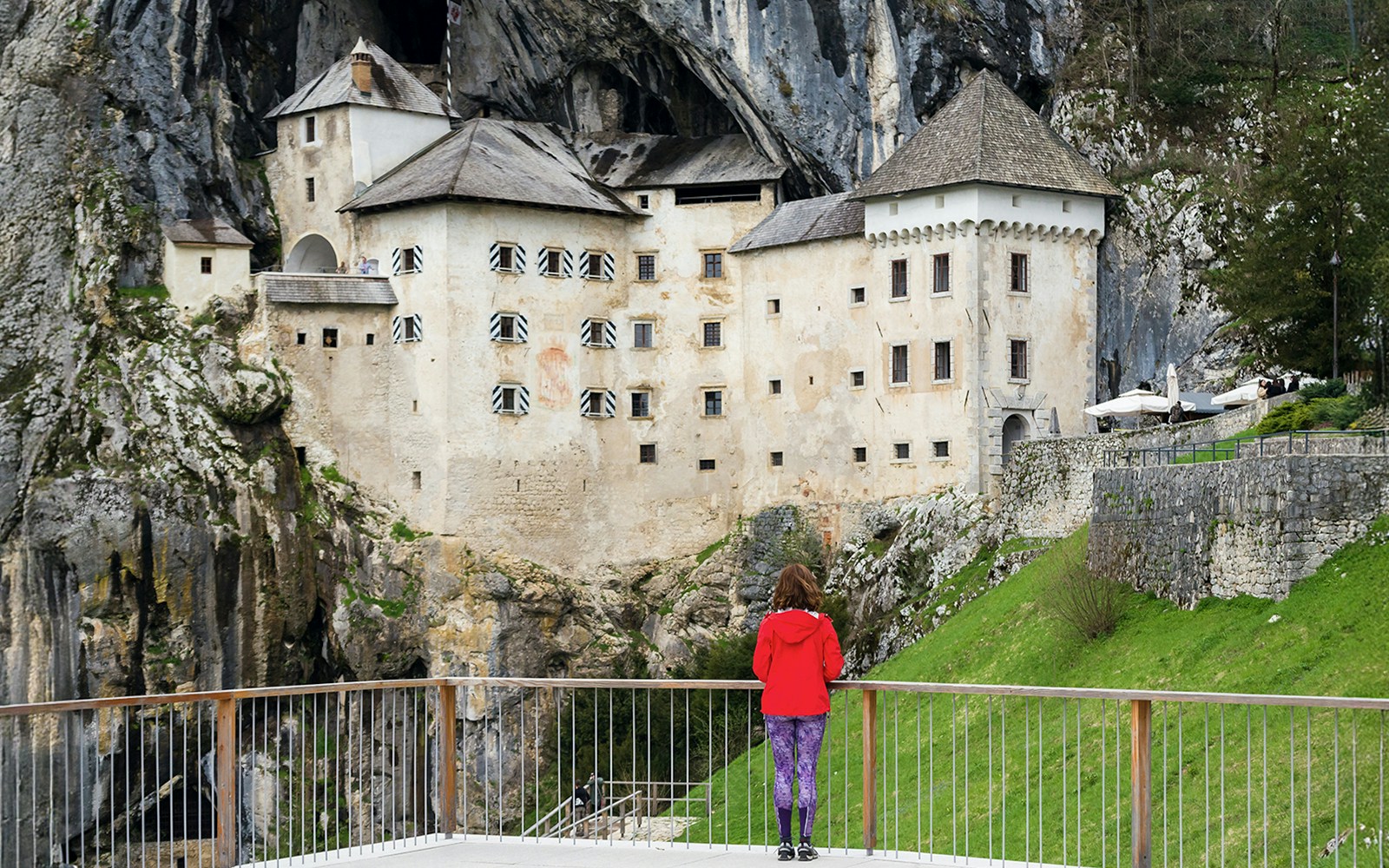 Predjama Castle built into a cliff with a visitor on the viewing platform.