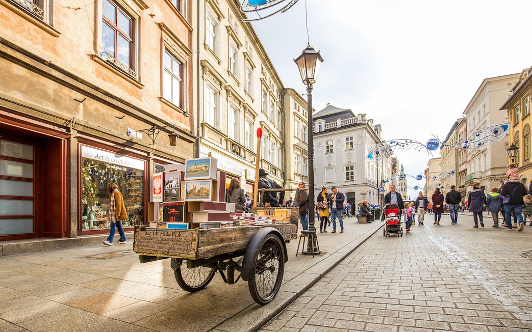 Street scene in Kraków's Old Town with market cart and pedestrians.