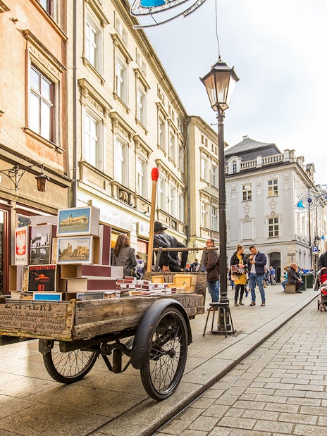 Street scene in Kraków's Old Town with market cart and pedestrians.