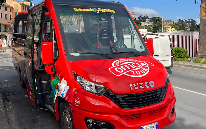 Red tour bus for day trip from Genova to Portofino parked on street.