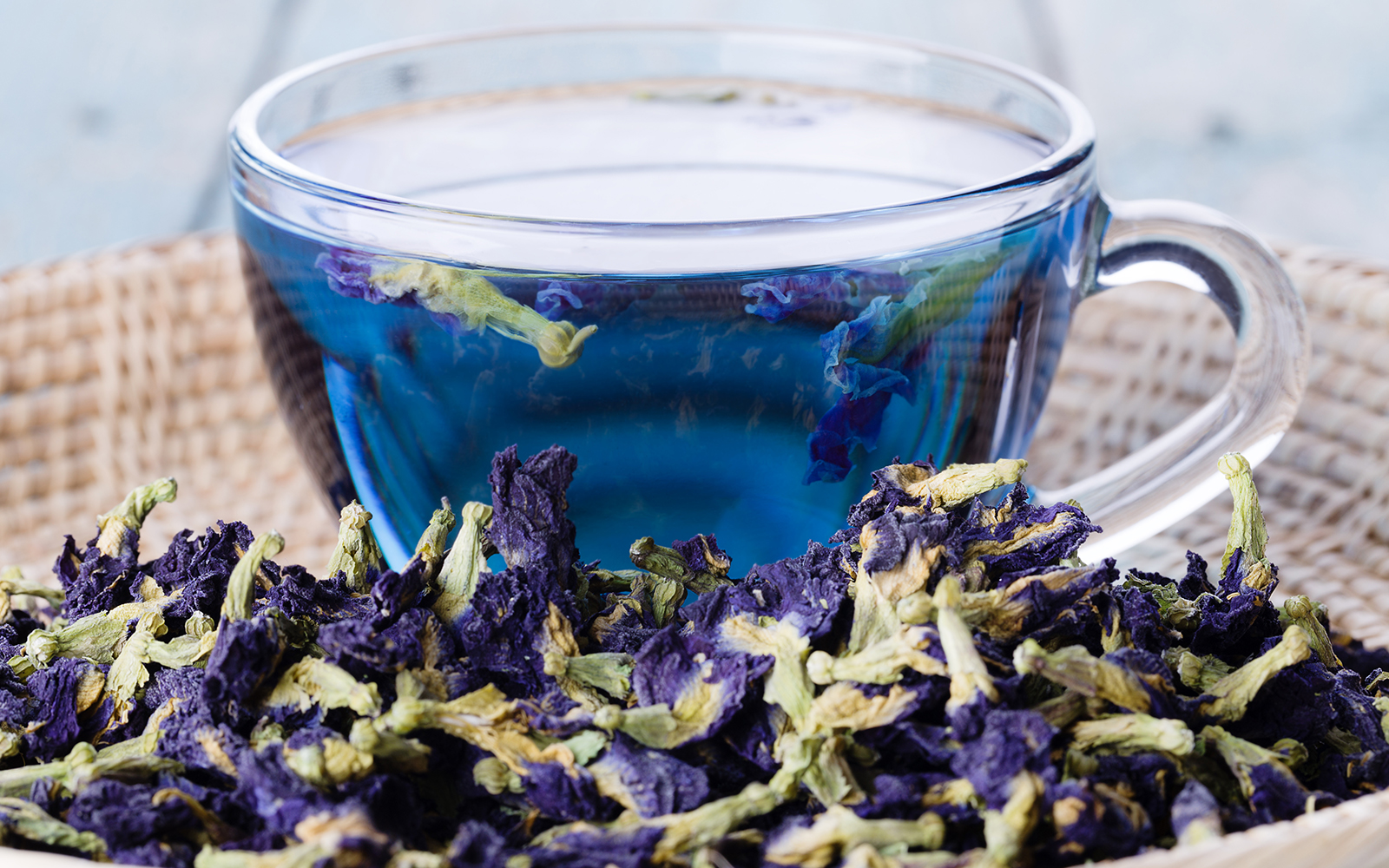 Cup of nutterfly pea flower tea served in a cup with a basket of butterfly pea flowers