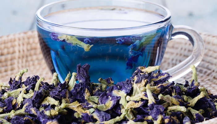 Cup of nutterfly pea flower tea served in a cup with a basket of butterfly pea flowers
