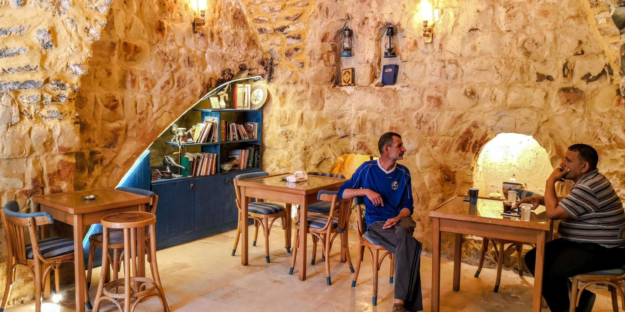 Two men seated in a rustic stone cafe in As-Salt, Jordan, enjoying a home-cooked lunch.