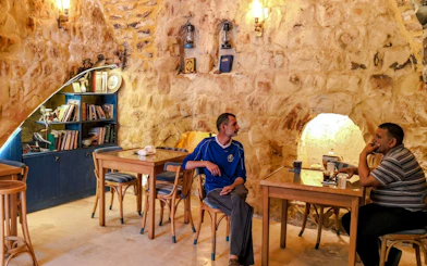 Two men seated in a rustic stone cafe in As-Salt, Jordan, enjoying a home-cooked lunch.