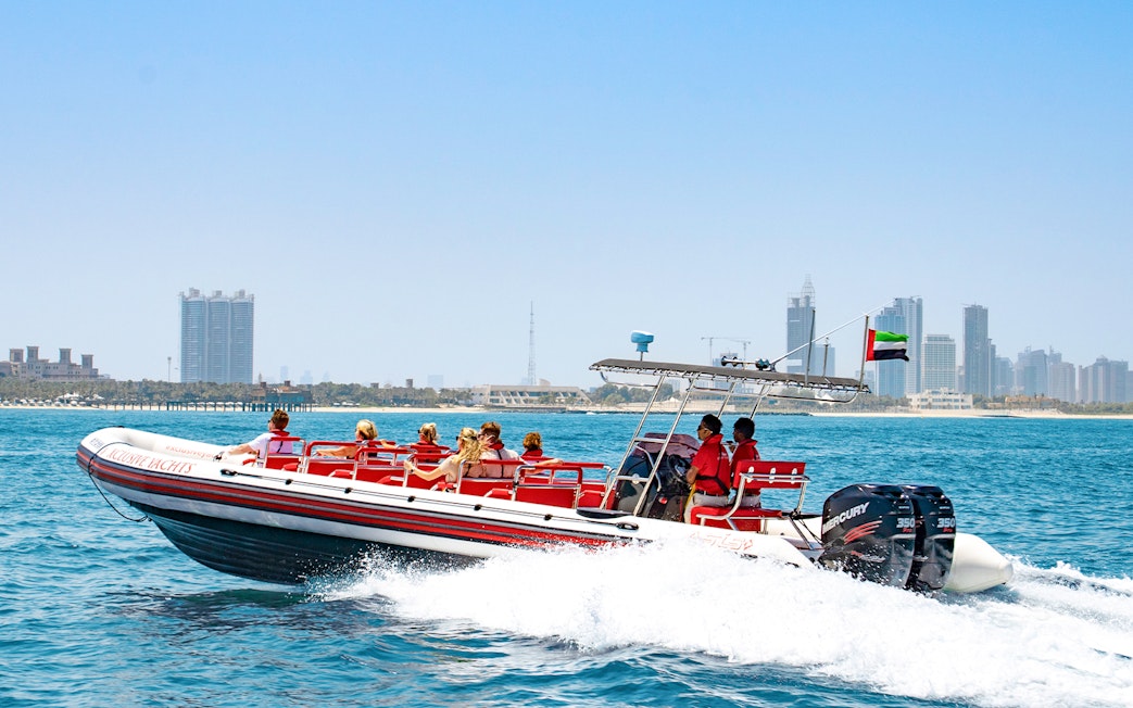Speedboat with tourists on Dubai Marina tour, city skyline in background.