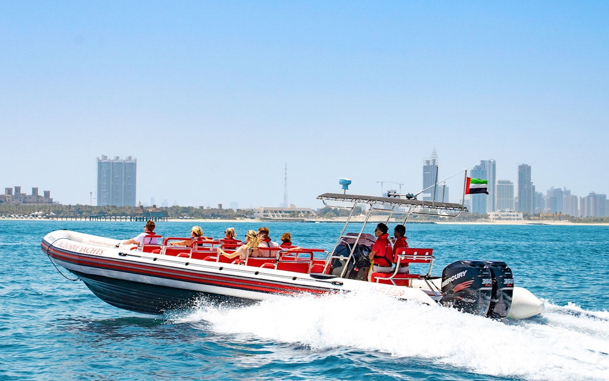 Speedboat with tourists on Dubai Marina tour, city skyline in background.