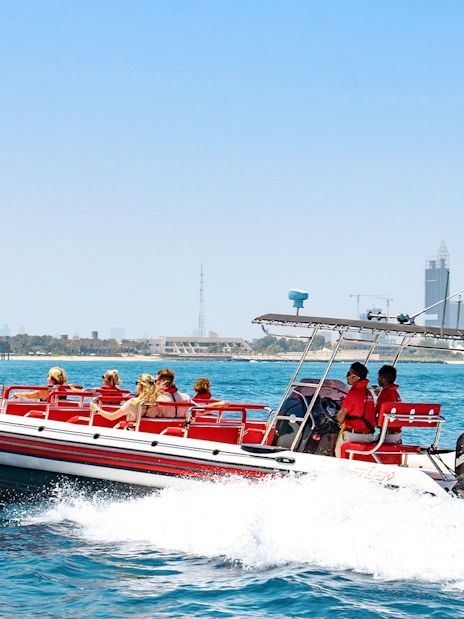 Speedboat with tourists on Dubai Marina tour, city skyline in background.