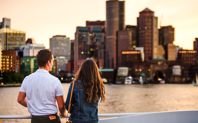 Guests enjoying a Boston sunset cruise with city skyline in the background.