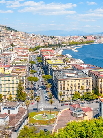 Aerial view of Naples coastline and cityscape, featuring historic buildings and the Gulf of Naples.