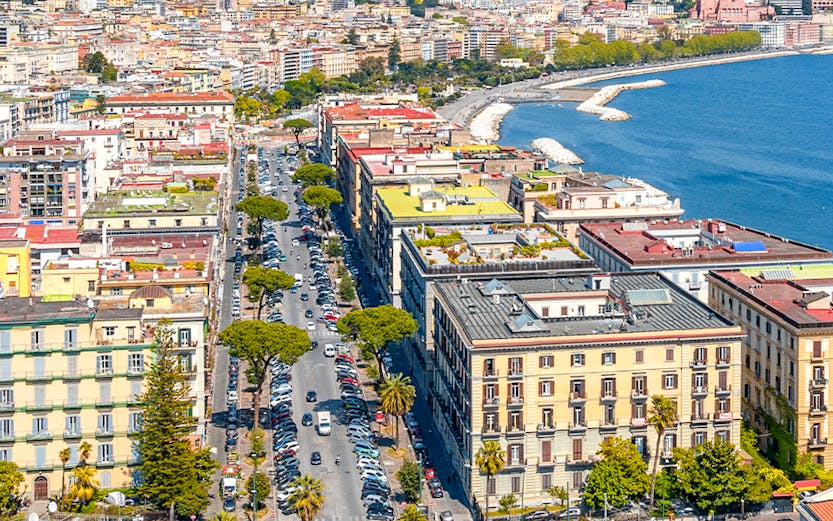 Aerial view of Naples coastline and cityscape, featuring historic buildings and the Gulf of Naples.