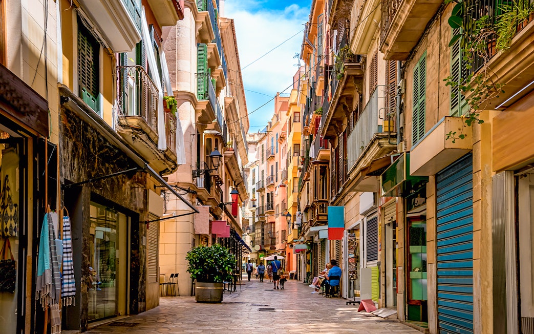 Narrow street in the shopping district of Palma de Mallorca with colorful buildings and people walking.