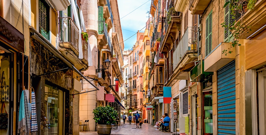 Narrow street in the shopping district of Palma de Mallorca with colorful buildings and people walking.