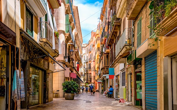 Narrow street in the shopping district of Palma de Mallorca with colorful buildings and people walking.