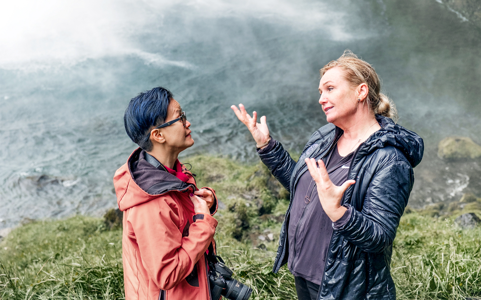 Two people discussing near a waterfall on the Glacier Lagoon & South Iceland Tour.