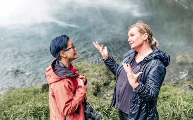 Two people discussing near a waterfall on the Glacier Lagoon & South Iceland Tour.