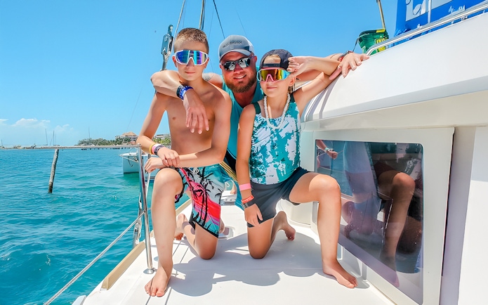 Family enjoying a catamaran trip in Isla Mujeres, with clear blue water in the background.