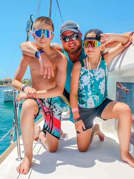 Family enjoying a catamaran trip in Isla Mujeres, with clear blue water in the background.