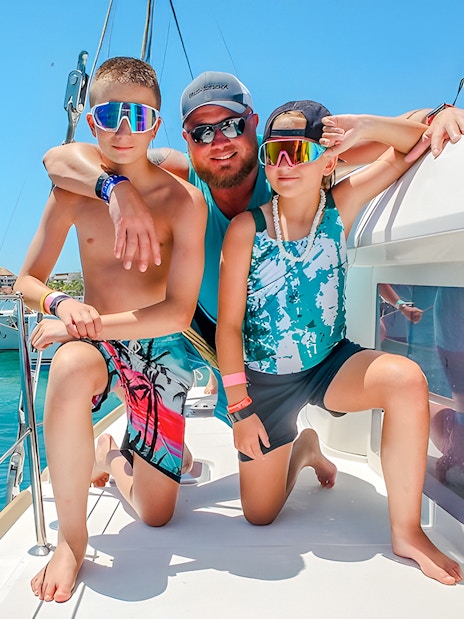 Family enjoying a catamaran trip in Isla Mujeres, with clear blue water in the background.