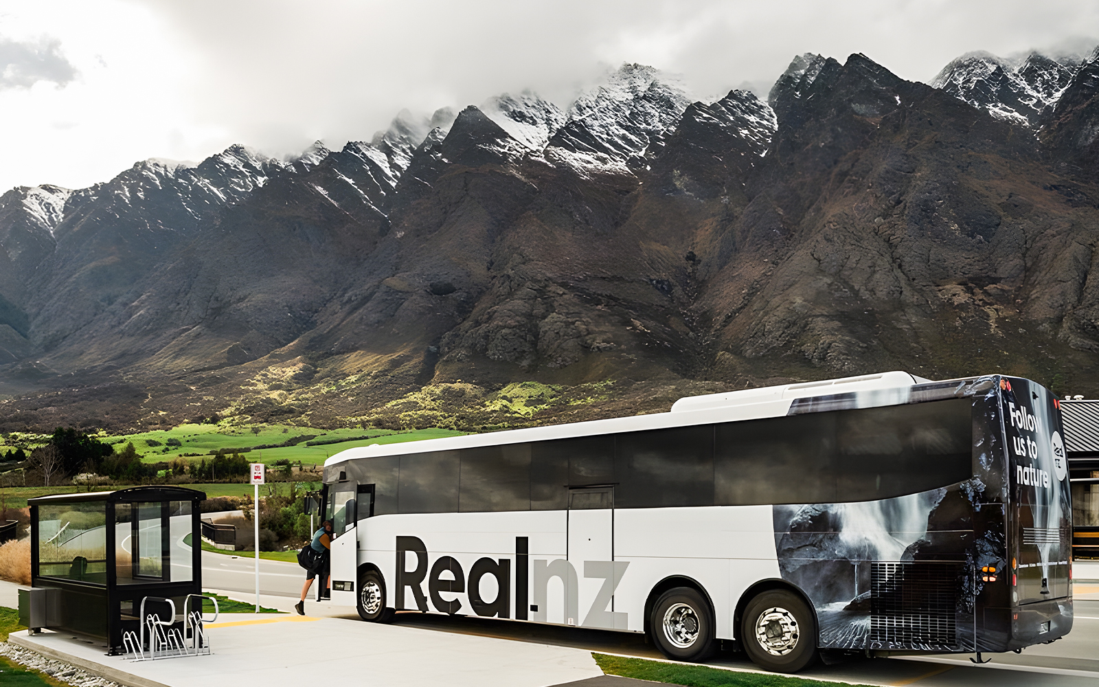 Bus at a stop with mountains in the background, Queenstown to Te Anau transfer.