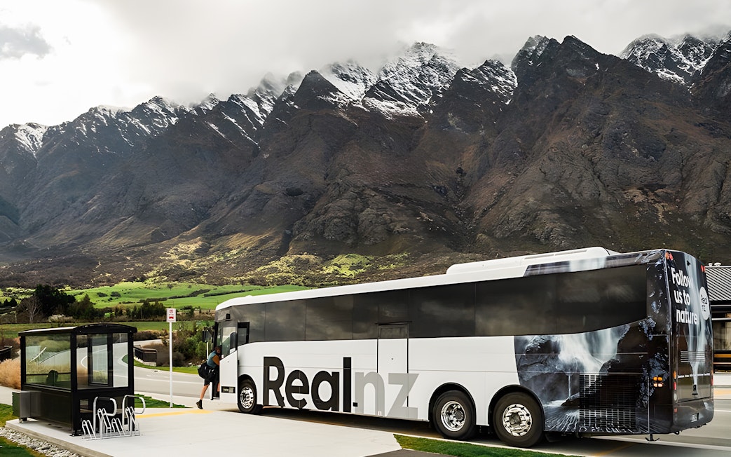 Bus at a stop with mountains in the background, Queenstown to Te Anau transfer.