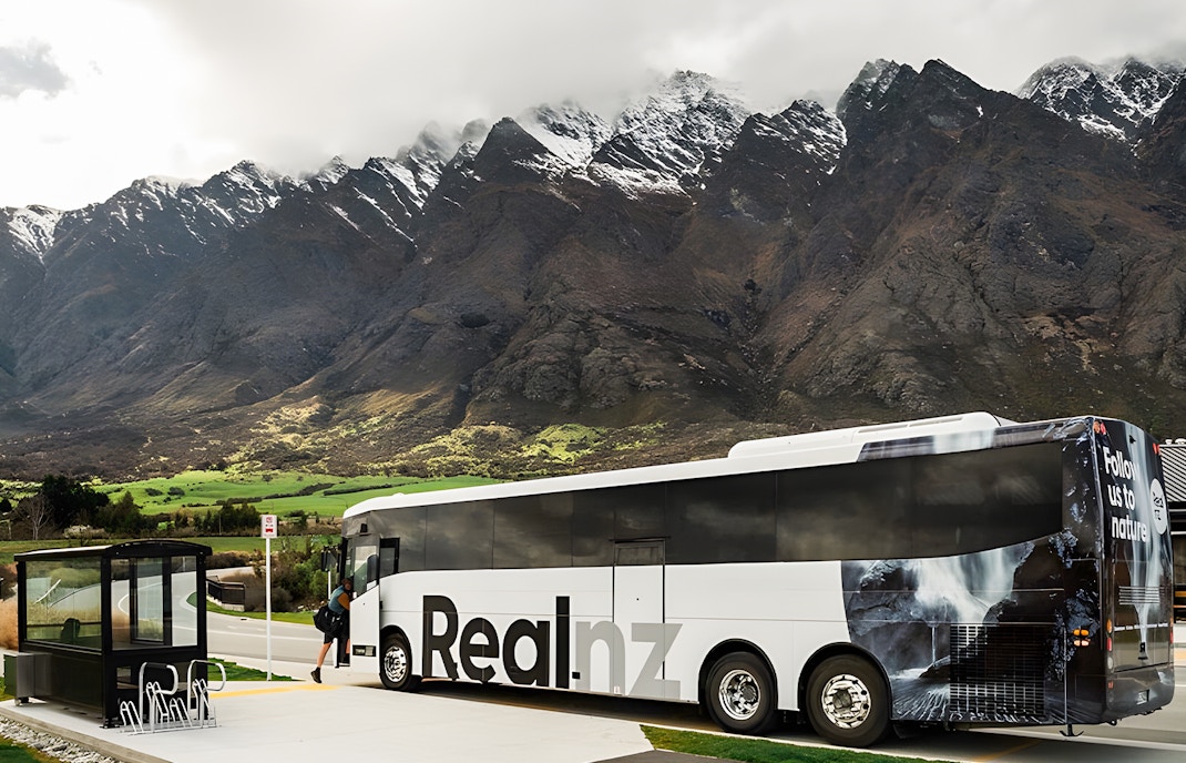 Bus at a stop with mountains in the background, Queenstown to Te Anau transfer.