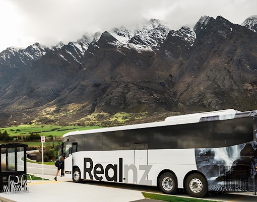 Bus at a stop with mountains in the background, Queenstown to Te Anau transfer.
