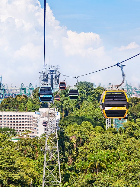 Cable cars over Sentosa Island with view of lush greenery and Singapore harbor.