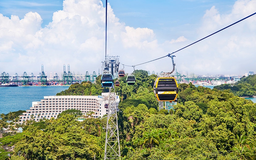 Cable cars over Sentosa Island with view of lush greenery and Singapore harbor.
