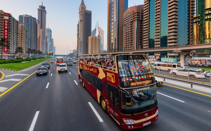 Open-top tour bus on Sheikh Zayed Road, Dubai, with skyscrapers in the background.