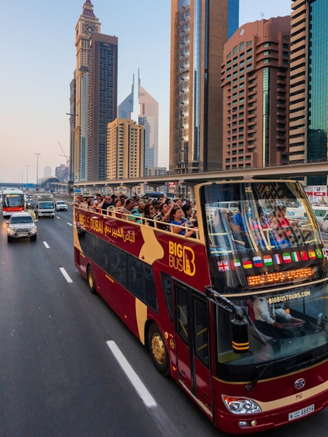 Open-top tour bus on Sheikh Zayed Road, Dubai, with skyscrapers in the background.