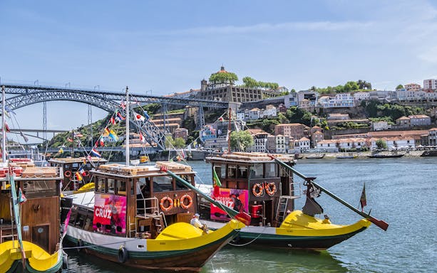 Traditional boats on Douro River with Dom Luís I Bridge and Porto cityscape in the background.