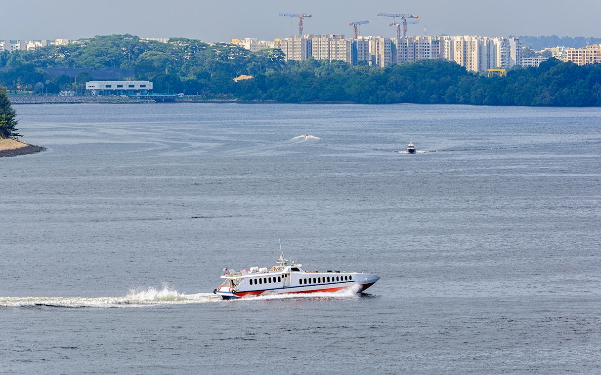 Ferry traveling across water with cityscape in background, Singapore to Desaru Coast route.