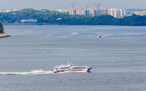 Ferry traveling across water with cityscape in background, Singapore to Desaru Coast route.