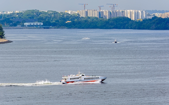 Ferry traveling across water with cityscape in background, Singapore to Desaru Coast route.
