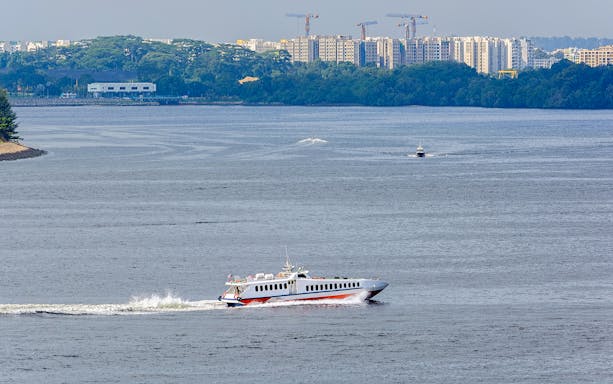 Ferry traveling across water with cityscape in background, Singapore to Desaru Coast route.