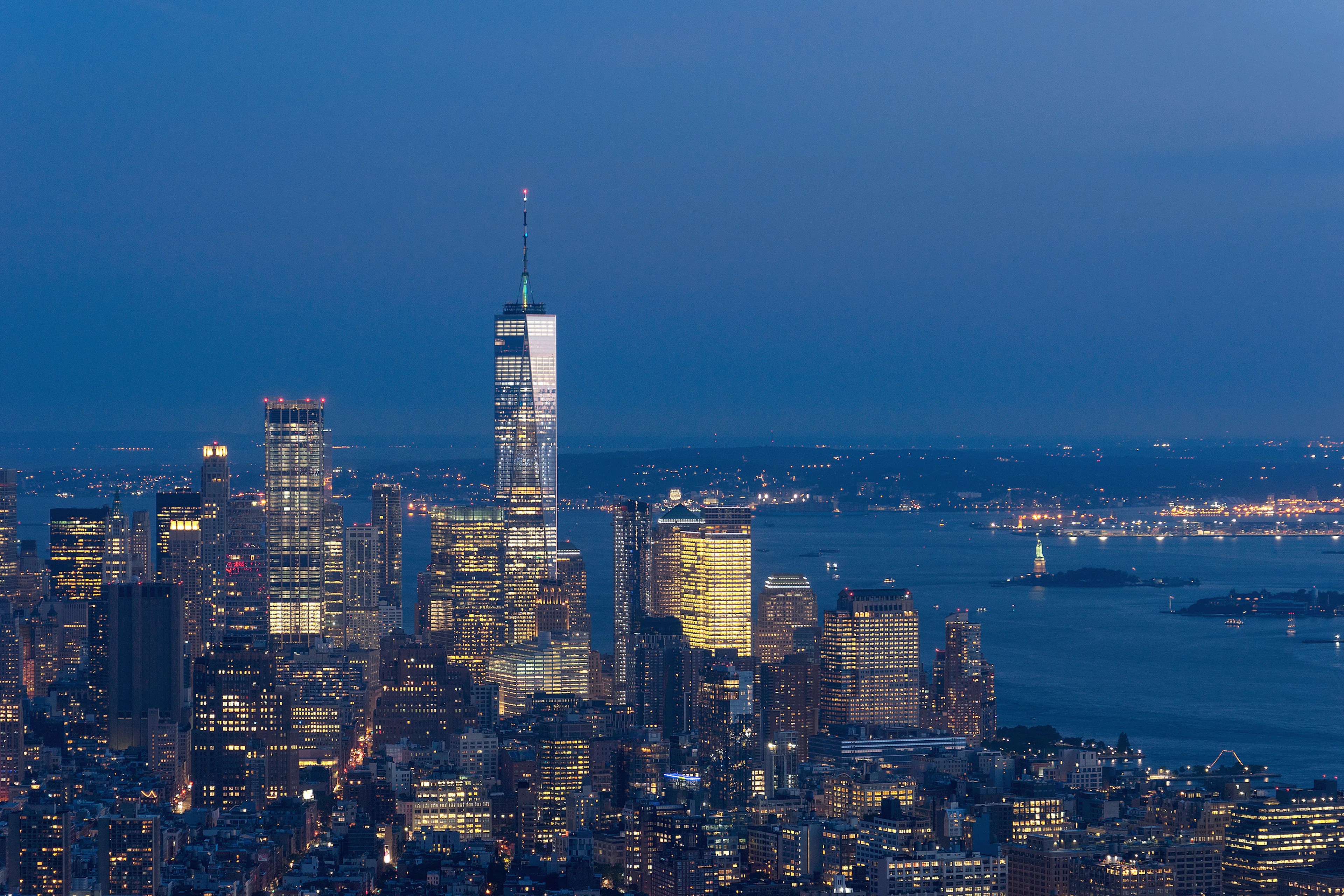 New York City skyline at night with One World Observatory and Statue of Liberty in view.