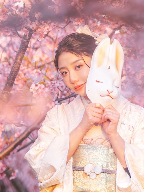 Kimono-clad person with fox mask under cherry blossoms at Kiyomizu Dera, Kyoto.