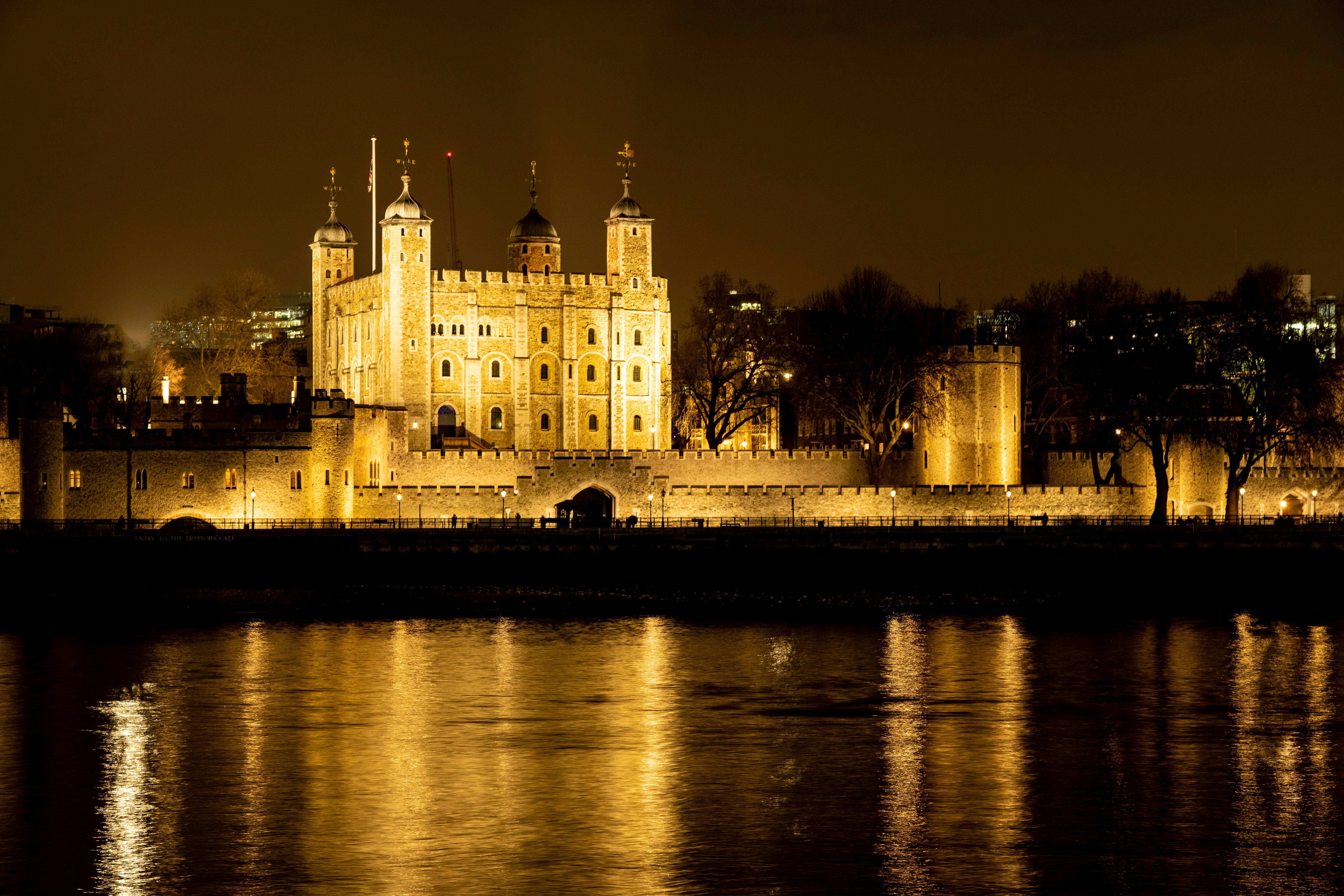 Tower of London illuminated at night, reflecting on the Thames River.